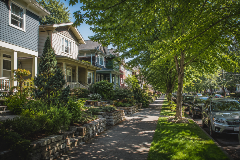 Rua arborizada de um bairro residencial em uma cidade americana, com casas, calçadas, jardins e veículos estacionados, ilustrando a organização típica de um bairro urbano.