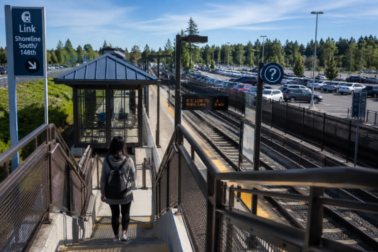 Passageira descendo para uma estação de trem ao lado de um estacionamento cheio de carros.