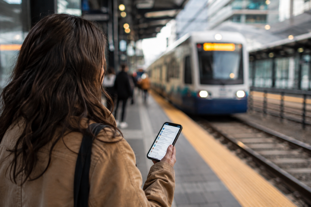 Passageira consulta horários no celular enquanto um trem se aproxima da plataforma.