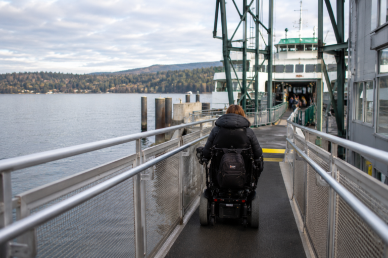 Pessoa em cadeira de rodas motorizada seguindo por uma rampa acessível em direção a uma balsa no Puget Sound.