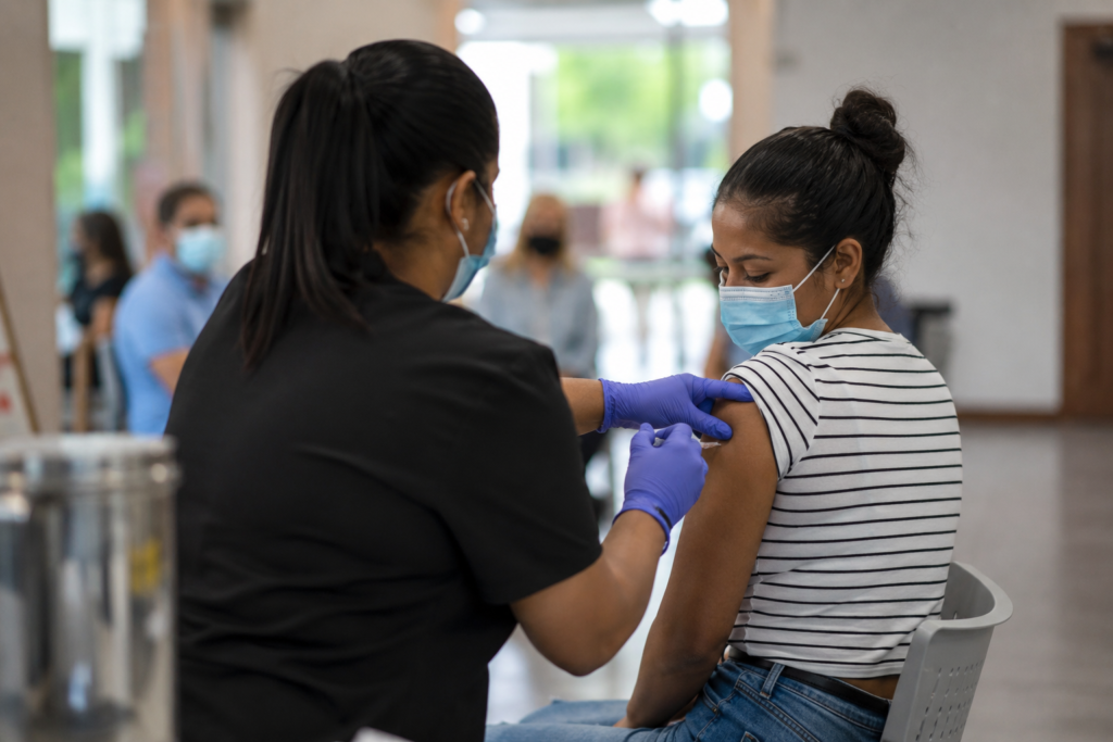 Profissional de saúde aplica uma vacina no braço de uma paciente em um ambiente comunitário de vacinação.