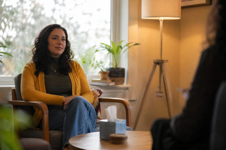 Mulher em uma consulta de saúde mental, sentada em uma poltrona e conversando com um profissional em um ambiente tranquilo e acolhedor.