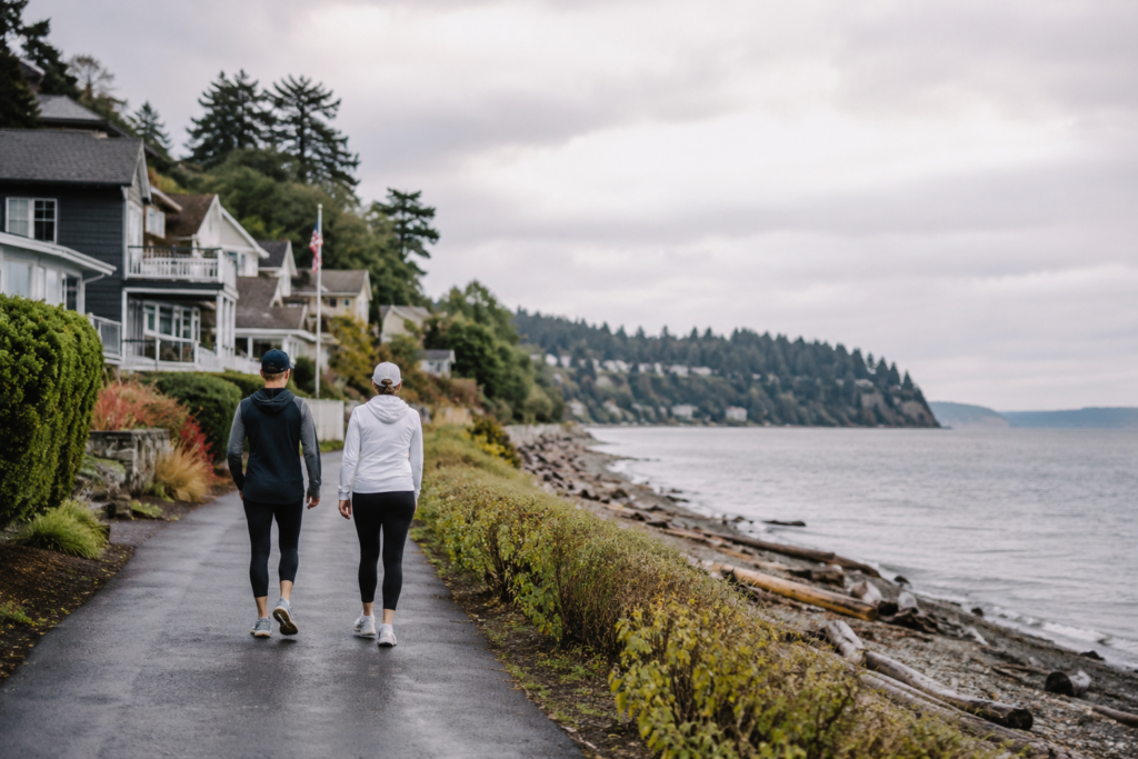 Duas pessoas caminhando à beira da água em uma área residencial do Puget Sound.