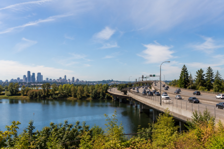 Faixa HOV em uma rodovia de Washington com vários veículos circulando sobre uma ponte, água e paisagem urbana ao fundo.