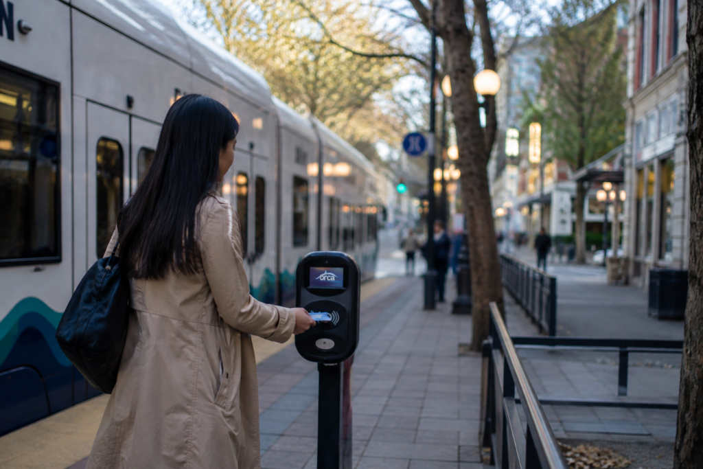 Passageira usando o cartão ORCA em um leitor de tarifas ao lado de um trem de transporte público na região de Puget Sound.