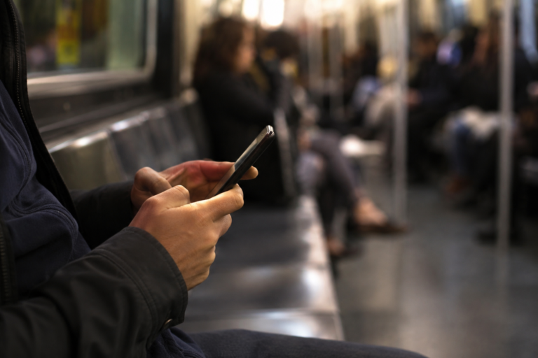 Pessoa utilizando o Zelle pelo celular durante um trajeto de transporte público, representando uma transferência bancária digital entre contas nos Estados Unidos.