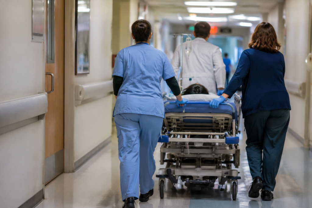 Equipe médica conduzindo um paciente em maca por um corredor hospitalar durante atendimento de emergência.