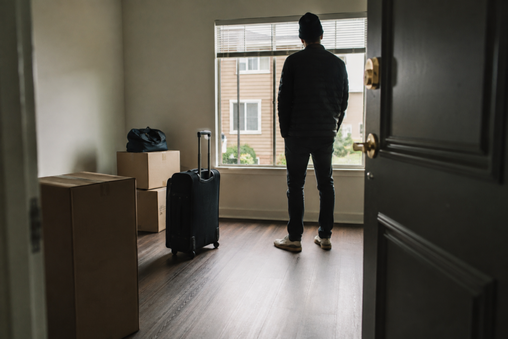 Pessoa em apartamento quase vazio, com caixas de mudança e mala prontas para a saída antes do fim do contrato de aluguel.