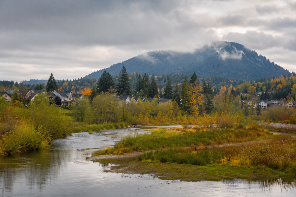 Issaquah Creek atravessando o vale, com áreas residenciais entre árvores de outono e montanhas florestadas cobertas por nuvens ao fundo.