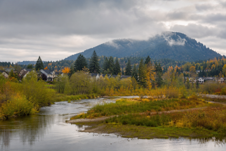 Issaquah Creek atravessando o vale, com áreas residenciais entre árvores de outono e montanhas florestadas cobertas por nuvens ao fundo.