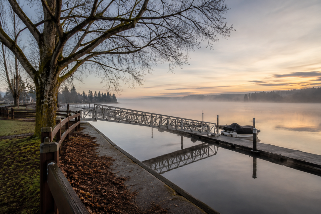Vista ampla do Lake Stevens ao amanhecer com marina silenciosa, águas calmas refletindo o céu e árvores típicas do noroeste do estado de Washington.