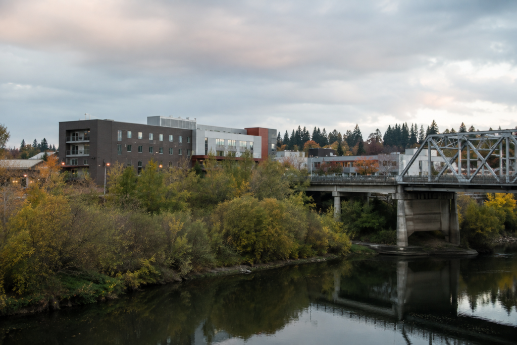 Vista ampla do rio Snohomish com a ponte histórica, vegetação ribeirinha e desenvolvimento urbano de Marysville ao fundo, retratando a ligação entre o centro da cidade, seus corredores de transporte e a paisagem natural do norte de Snohomish County.