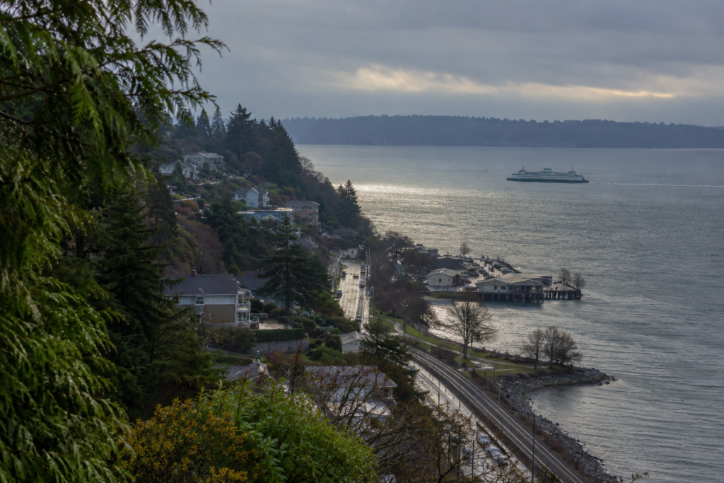 Vista elevada de Mukilteo com bairros na encosta, ferrovia junto à costa e balsa atravessando o Puget Sound em direção a Whidbey Island.
