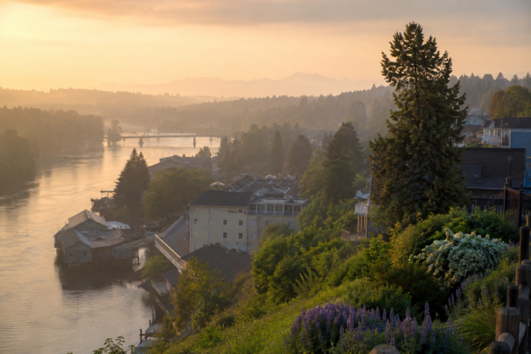 Vista elevada do centro histórico de Snohomish ao amanhecer, com o rio Snohomish contornando edifícios preservados, vegetação abundante e o amplo vale ao fundo, destacando a transição entre a cidade histórica e a paisagem rural do condado.