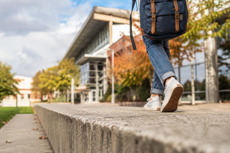Estudante caminhando com mochila por um campus universitário em um dia de outono.