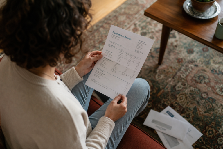 Pessoa analisando uma explicação de benefícios do plano de saúde em casa, com documentos e correspondências sobre a mesa.