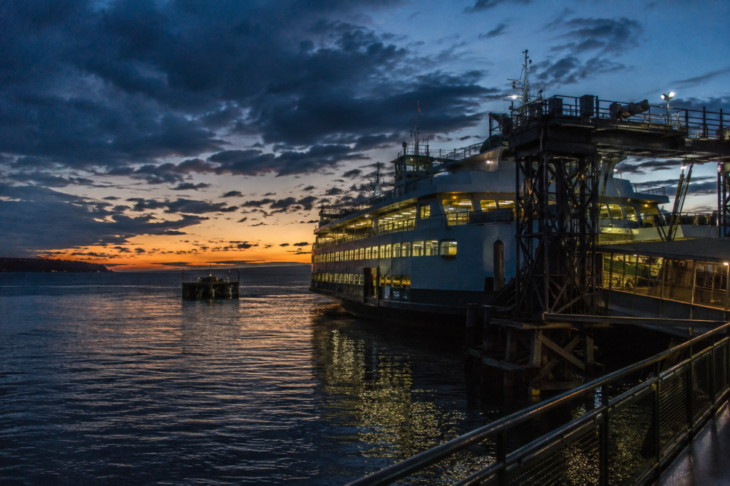 Balsa atracada em terminal no Puget Sound ao entardecer, com infraestrutura portuária iluminada e águas da região ao fundo.