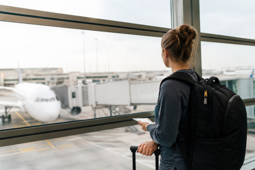 Passageiro com mochila observando um avião pela janela de um terminal de aeroporto antes de um voo doméstico nos Estados Unidos.